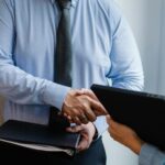 Business handshake between colleagues in a formal office meeting setting.